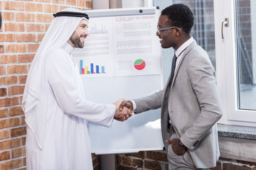 Multiethnic businessmen shaking hands near white board in office