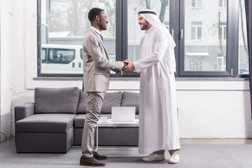 african american businessman and arabic business partner standing and shaking hands in office