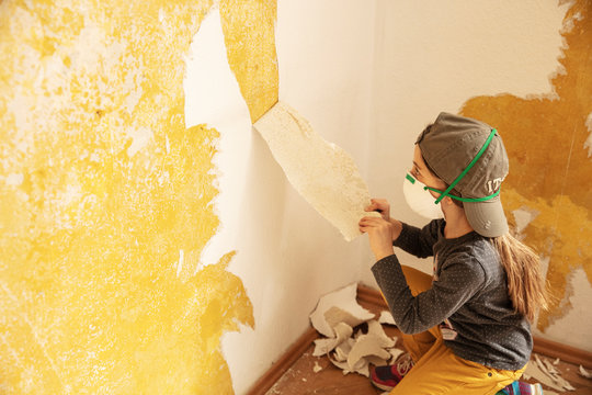 Young girl stripping wallpaper from old wall. Munich, Germany
