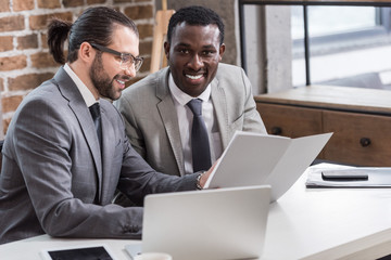 handsome businessman reading document while african american partner looking at camera in office