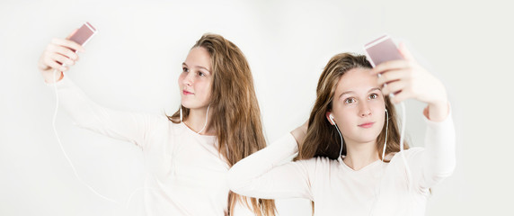 beautiful young twins taking a selfie on the phone in headphones on a white isolated background