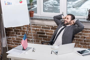 successful businessman with hands on head sitting in modern office