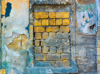 Window opening laid with yellow stones in the old wall covered with many layers of colored stucco and partially destroyed under the influence of time and weather