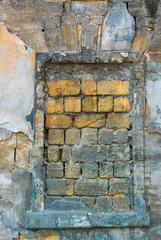 Vertical photo of the window opening laid with yellow stones in the old wall covered with many layers of colored stucco and partially destroyed under the influence of time and weather