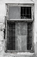 Black and white photo of an old window frame with partially broken windows and metal bars inside the old dilapidated wall