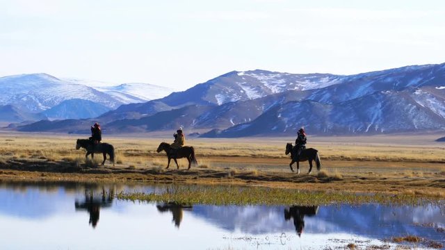 ULGII, MONGOLIA - OCTOBER 9, 2018 : Mongolian Eagle Hunters with the well trained eagle hunter on their arm riding horseback pass the lake in the steppe at Ulgii in Mongolia