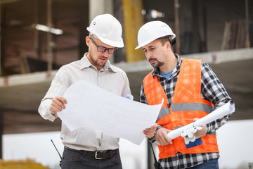 Male architect and developer discussing blueprints at construction site