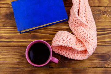Cup of coffee, knitted scarf and book on wooden background
