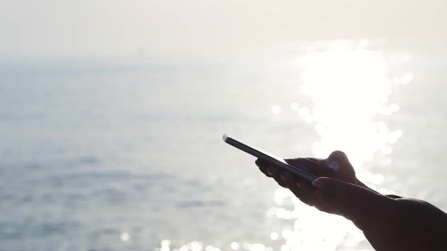 Closeup profile view of beautiful adult female hands holding modern smartphone Isolated at golden sunrise sea water background. Woman typing messenger using touchscreen.