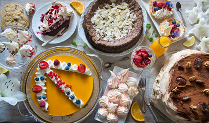 Table with loads of cakes, cupcakes, cookies, cakepops, desserts, fruits, flowers and orange juice.