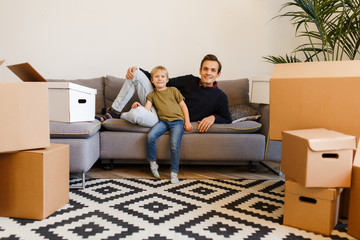 Image of happy father and son sitting on gray sofa among cardboard boxes