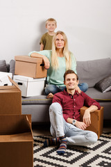 Photo of parents with their son sitting on gray sofa with cardboard boxes