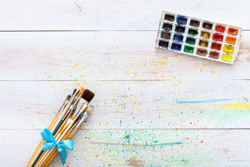 Paint brushes set and box with watercolors on white wooden stained table with splashes, artistic...
