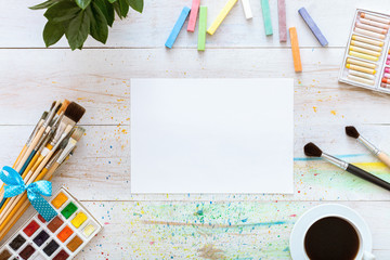 Paint brushes, paintbox with watercolors, crayons, coffee and blank mock up paper on white wooden...