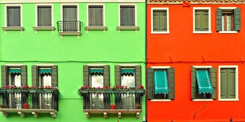 Beautiful windows with green shutters and balcony with flowers on red and green wall. Colorful houses on Burano island near Venice, Italy