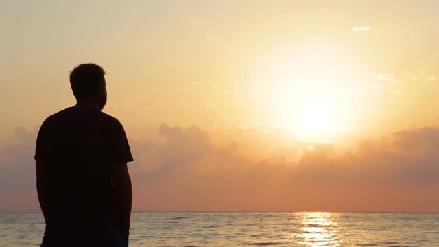 Black silhouette of adult man isolated at beautiful marine sunrise golden landscape background. Real time full hd video footage.