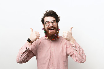 Happy man in casual with decorated christmas beard showing thumbs up and smiling over white...