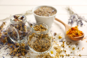 Glass jars with dried flowers on white wooden table
