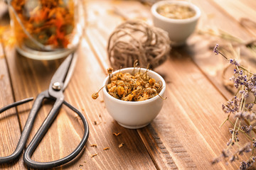 Bowl with dried chamomile flowers on wooden table