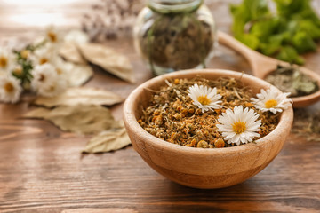 Bowl with dried chamomile flowers on wooden table - obrazy, fototapety, plakaty