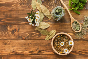 Fototapeta na wymiar Bowl with dried chamomile flowers and herbs on wooden table