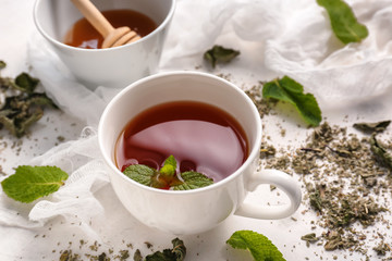 Cup of hot tea and dried mint on light table