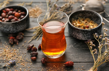 Glass of hot tea with dried flowers and rose hips on wooden table