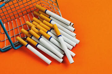 Market basket and cigarettes with filter dropped on orange background with copy space for your text or logo. Business concept