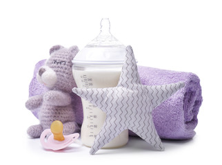 Feeding bottle of baby formula with toys and towel on white background