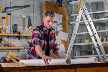 A carpenter works. Carpenter studying drawing project. Against the background of the workshop