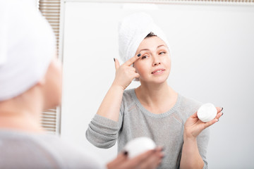 Smiling aged woman applying anti-aging cream. Happy mature woman using cosmetic cream to hide wrinkles.