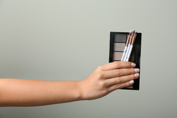 Woman holding eyeshadows with makeup brushes on grey background