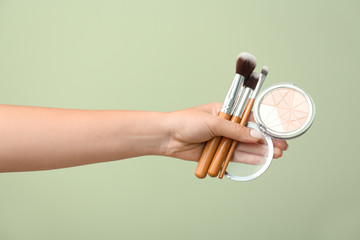 Woman holding powder with makeup brushes on color background