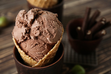 Waffle cone with delicious ice cream in cup on table