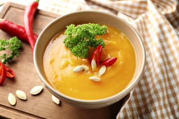 Bowl with tasty pumpkin cream soup on wooden board
