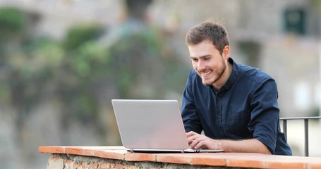 Happy man typing on a laptop in a balcony of a rural apartment - Powered by Adobe