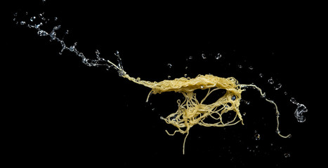 Noodles with soup splash or explosion flying in the air over dark background