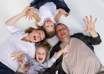 Top view of parents, their cute little daughters holding hands up, looking at camera and smiling and laughing shouting, lying on gray floor. Family holiday and togetherness.