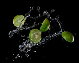 Fototapeta na wymiar Limes with water splash or explosion flying in the air isolated on black background