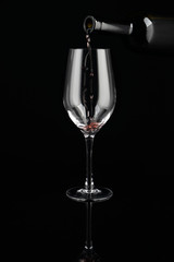 Pouring of red wine from bottle into glass on dark background