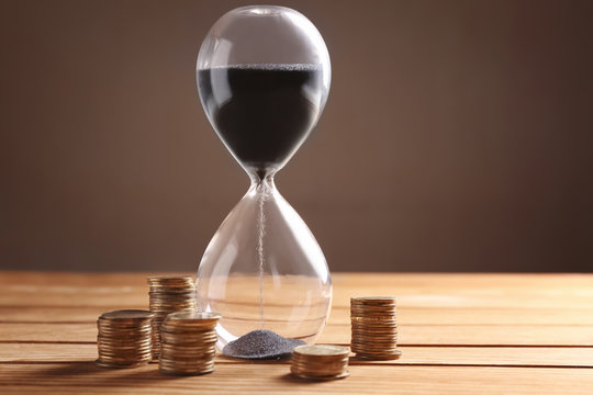 Crystal Hourglass With Black Sand And Coins On Wooden Table. Time Is Money