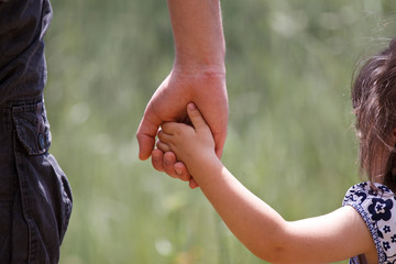 Dad holding his little girl's hand with nature at background.