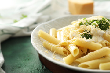 Plate with tasty penne pasta and cream sauce on color table