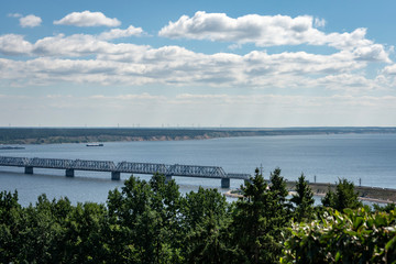 Fototapeta premium Old Imperial Bridge over the Volga River in Ulyanovsk. Bridge was built in 1916. Green banks and blue smooth surface of the river.