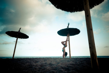 itness position for beautiful body fitness young woman girl at the beach use umbrella sun for reverse exercise - sea and sky with horizon in background - wellness and healthy millennial people