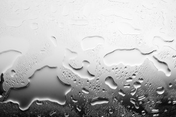 Monochrome black and white image of spilled water, glass surface in drops of water, gray gradient, abstract background, backdrop for banner, poster, wallpaper, condensate drops on glass close up macro