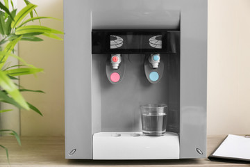 Modern water cooler with glass on wooden table