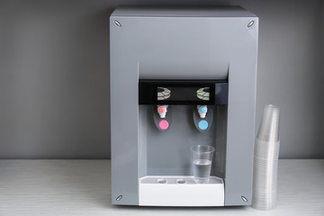 Modern water cooler with plastic cups on white table