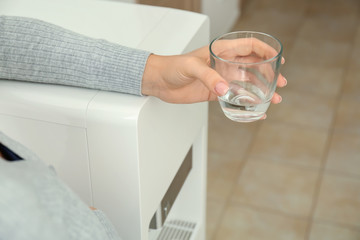 Woman with glass of water near cooler in office