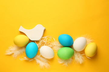 Easter eggs with bird toy and feathers on color background